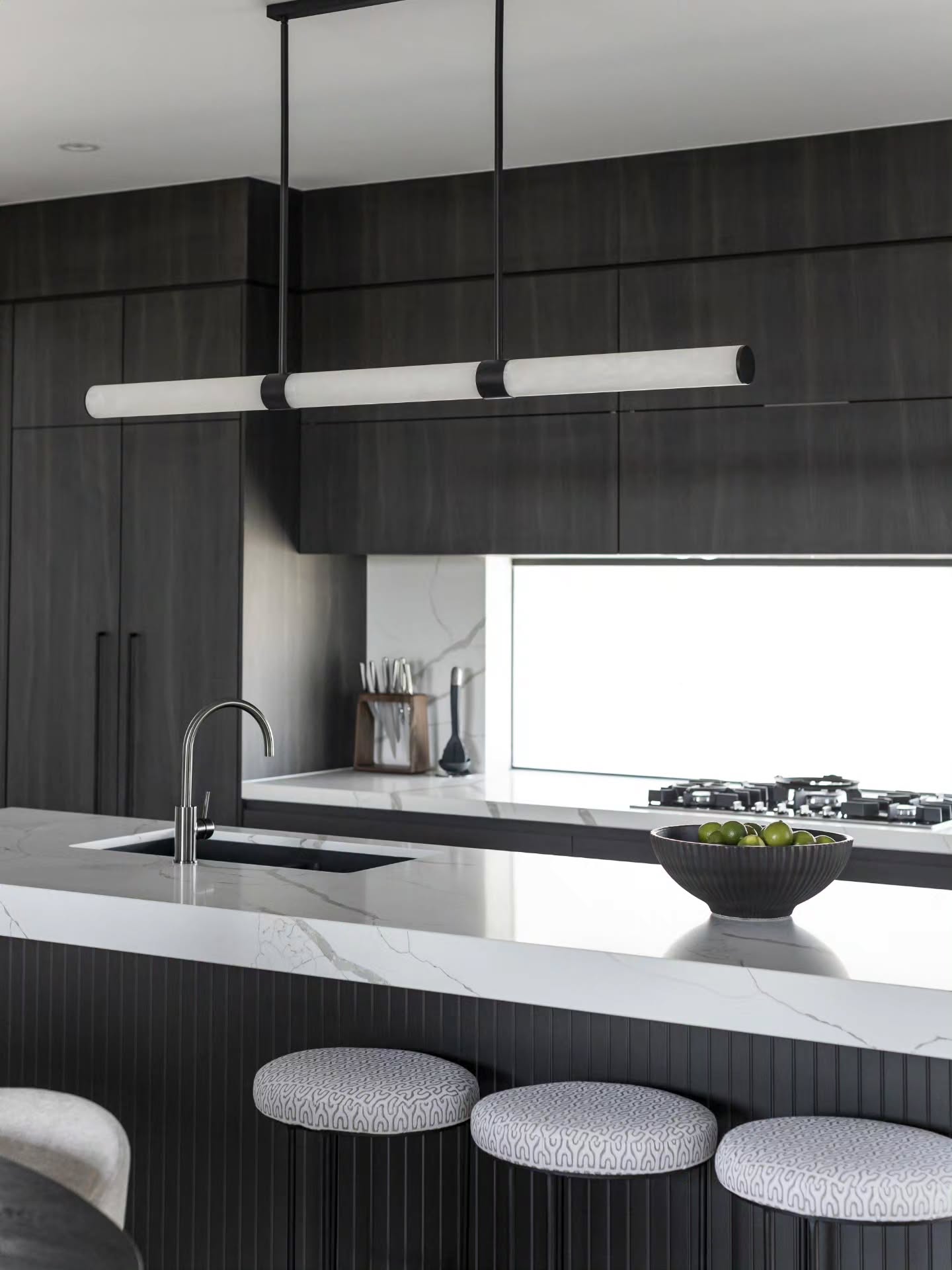 Marble breakfast bar with patterned stools and a linear tube pendant over a fluted black base — Monochrome Residence