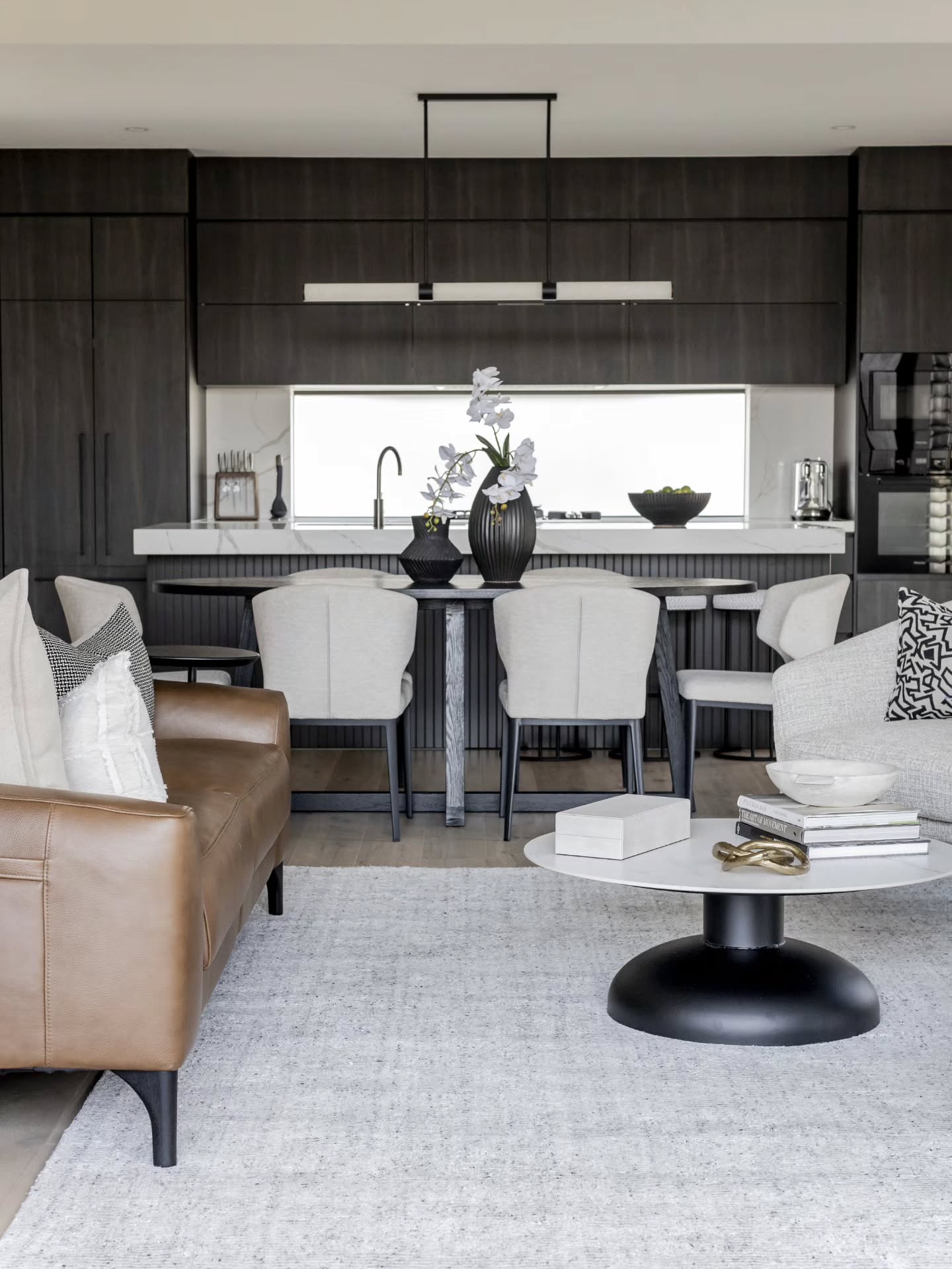 Living room with a tan leather sofa and the dining area and kitchen beyond — Monochrome Residence