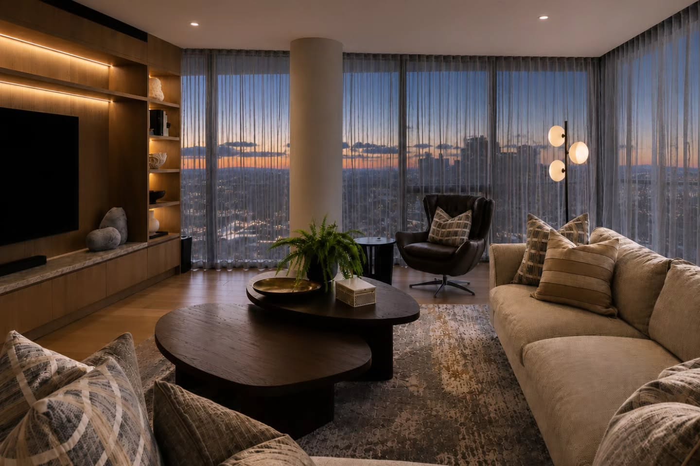 Living room at dusk with sheer curtains, city skyline and an oval timber coffee table — Oceanfront Apartment